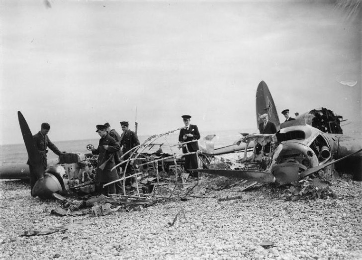 2 Civilians and RAF personnel search through the burnt-out remains of a Heinkel He 111 which crashed on a south coast beach, 11 July 1940